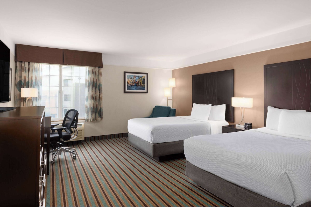 A hotel room with two beds, a desk, a chair, and a window with curtains.