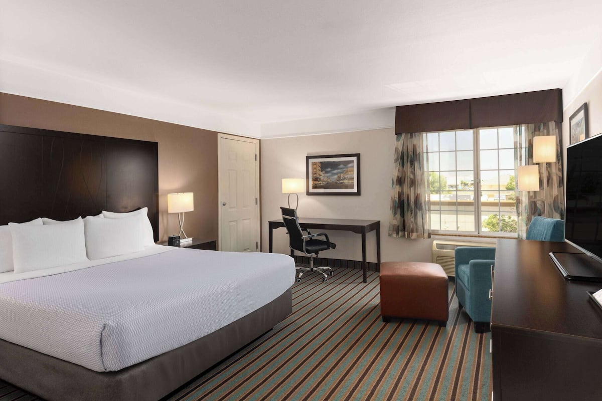 A hotel room with a large bed, a desk with a chair, a television, and a window with curtains.