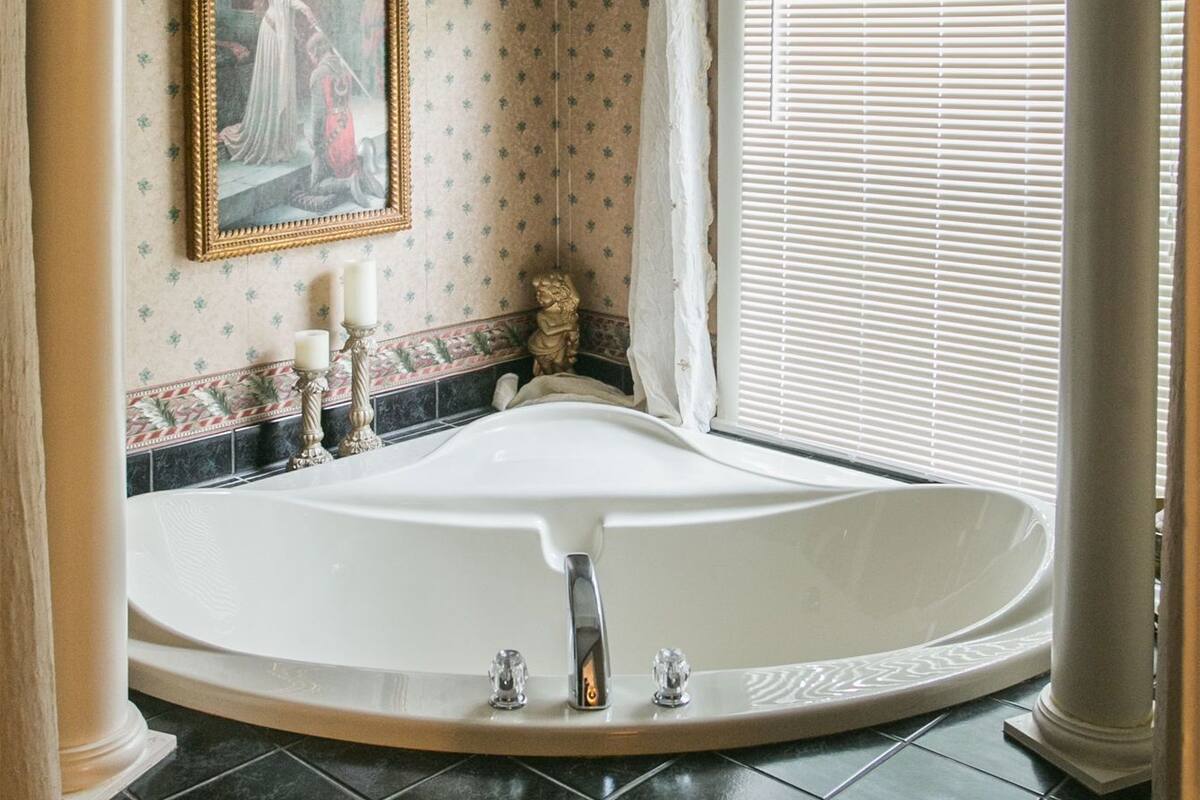 A bathroom with a large bathtub, a painting on the wall, and a window with blinds.