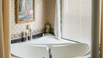 A bathroom with a large bathtub, a painting on the wall, and a window with blinds.