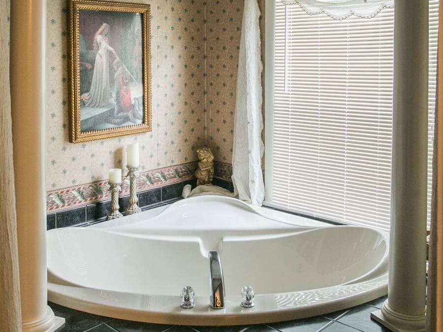 A bathroom with a large bathtub, a painting on the wall, and a window with blinds.