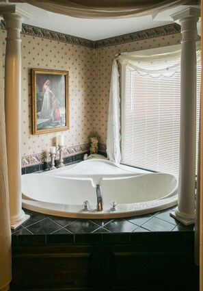 Une salle de bain avec une grande baignoire, un tableau au mur et une fenêtre avec des stores.