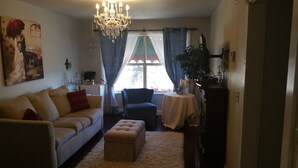 A living room with a sofa, ottoman, chandelier, and a table with a plant. - Woodstock Inn B&B (Independence)