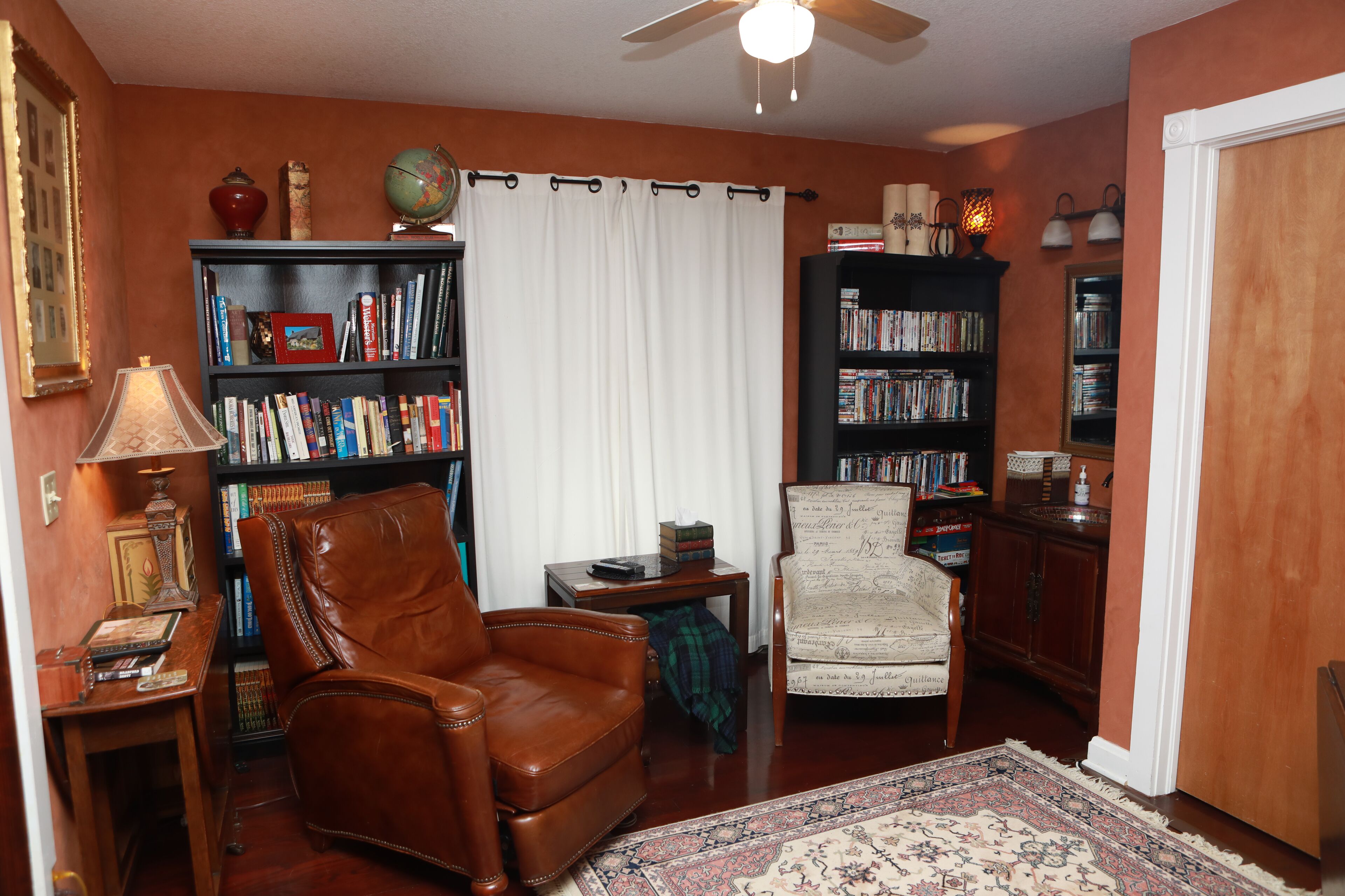 Un salón con un sillón de cuero marrón, un tapete estampado y dos estanterías llenas de libros y objetos decorativos.