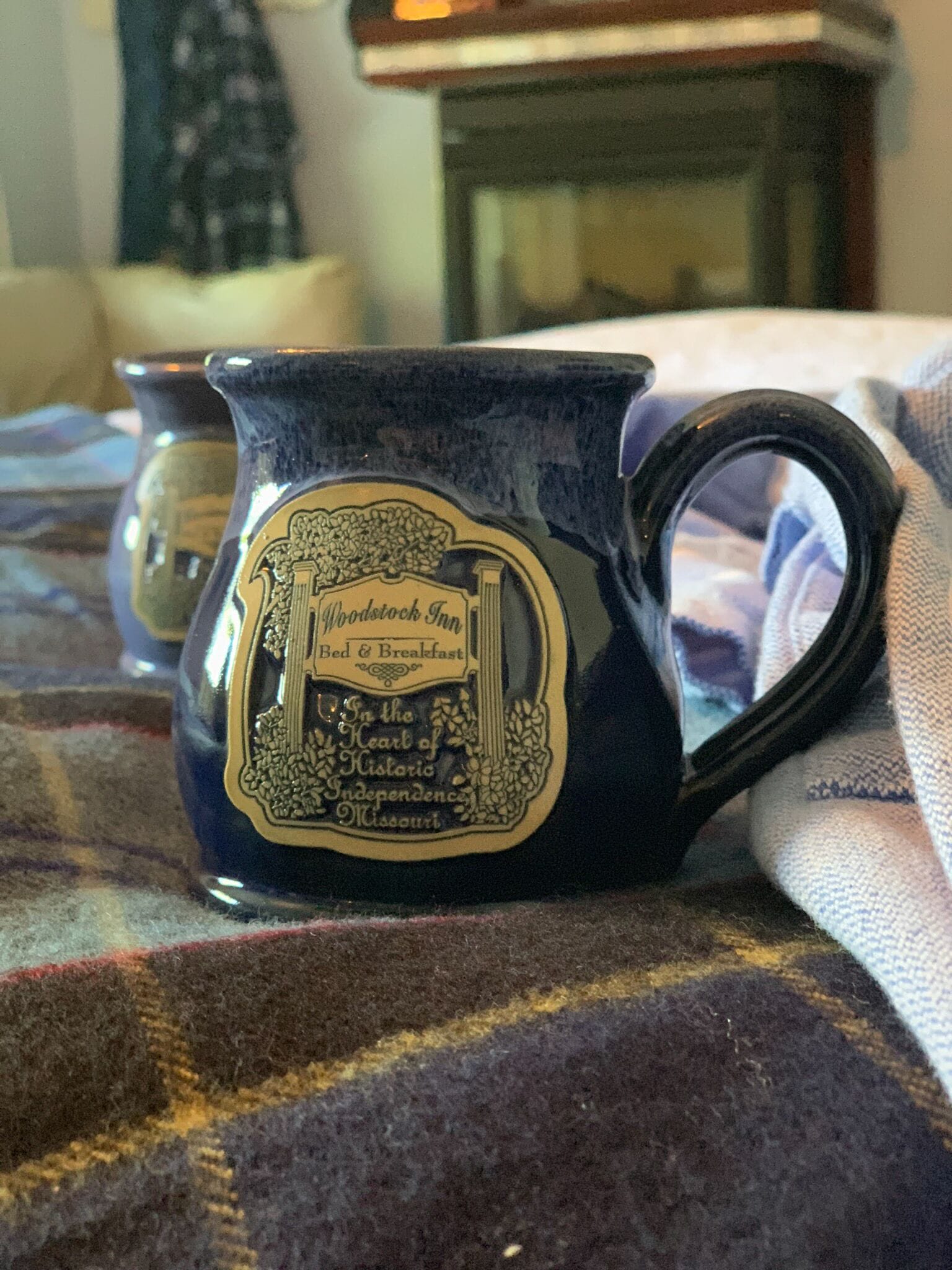 Una taza de cerámica azul con un emblema decorativo y texto, sobre una superficie de tela escocesa.