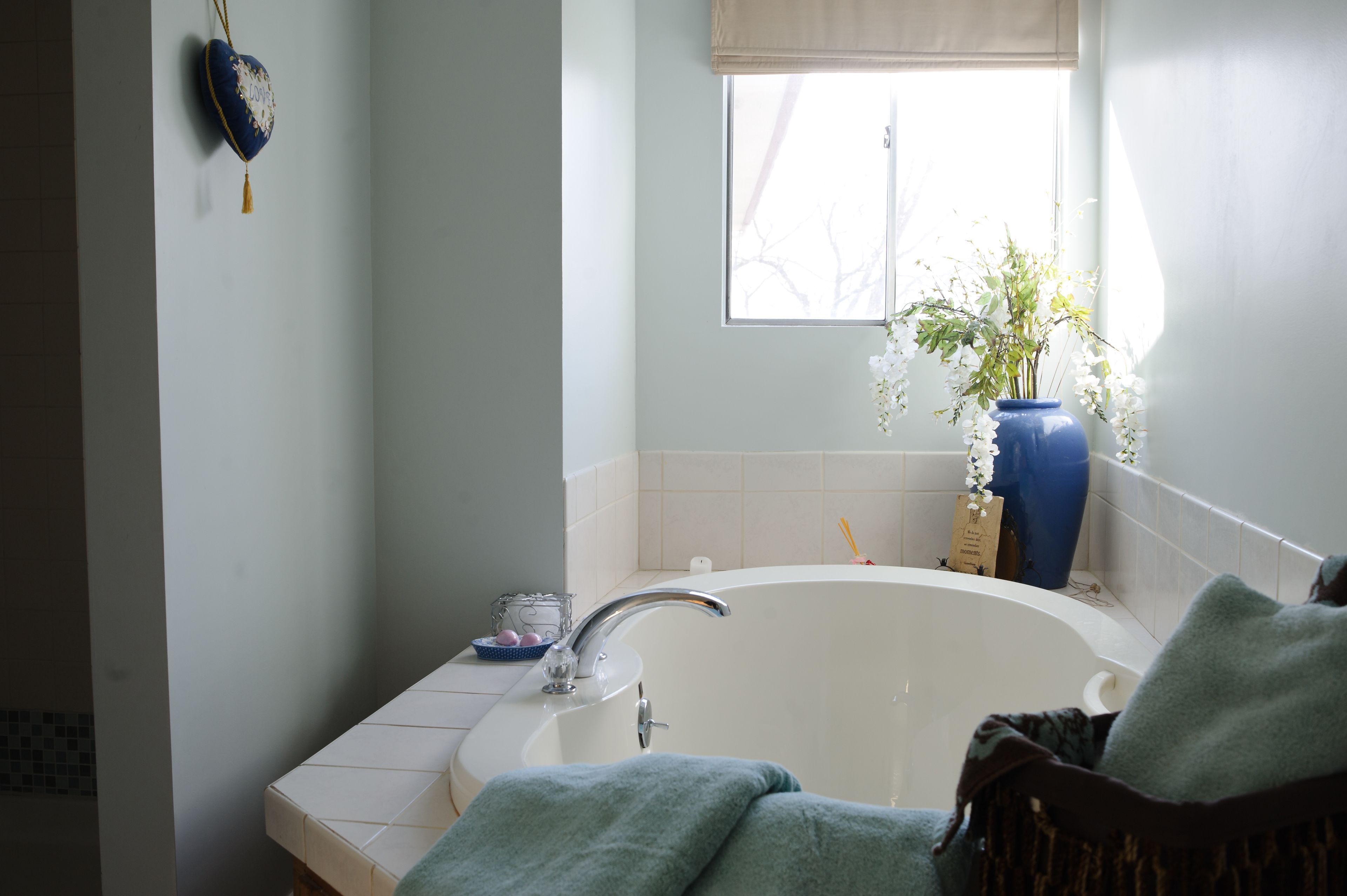 Un baño con bañera, ventana y un florero con flores.