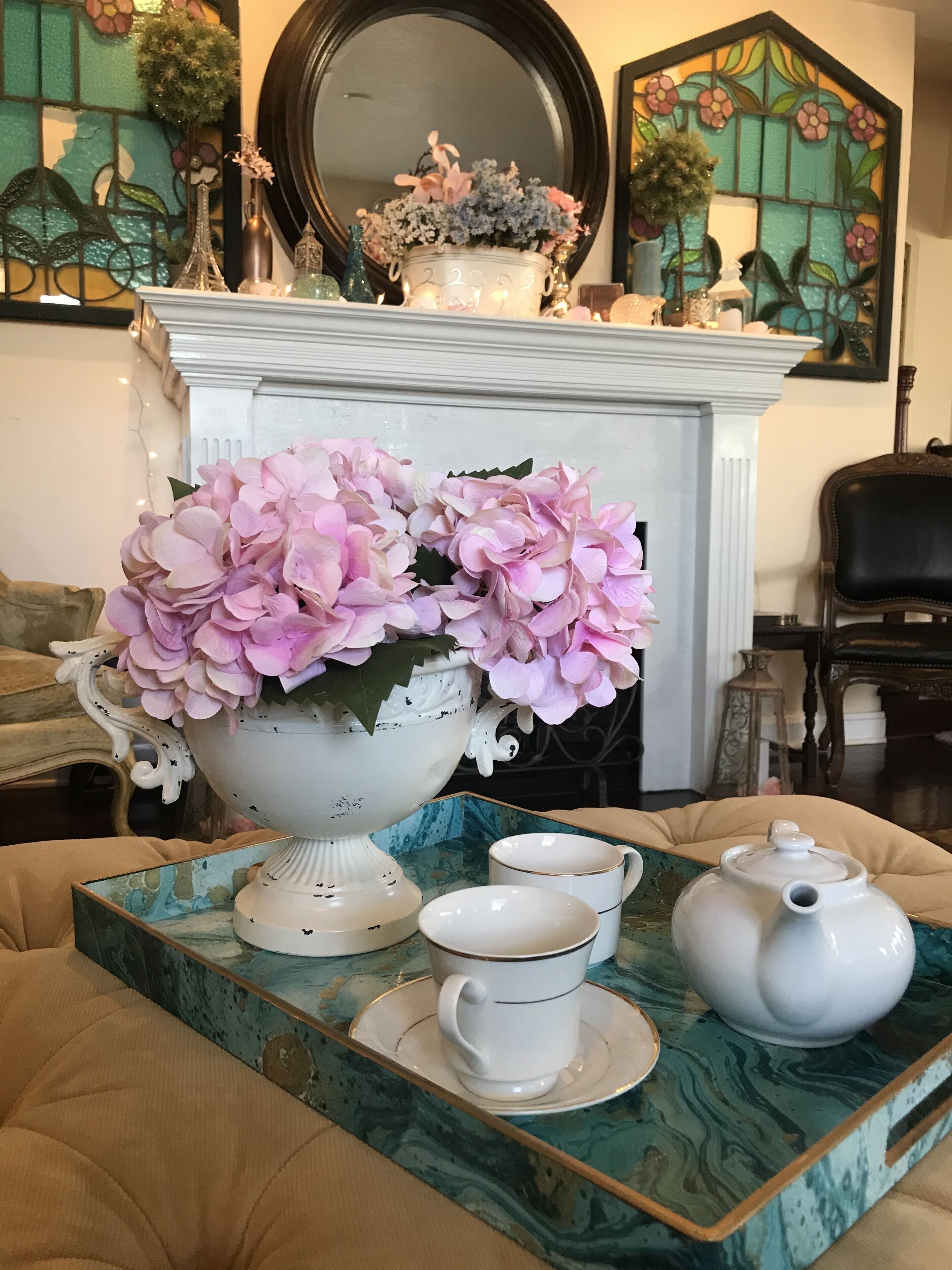 A decorative table with a white teapot, a cup, and a saucer, and a large vase with pink flowers.