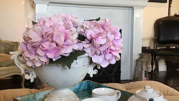 A decorative table with a white teapot, a cup, and a saucer, and a large vase with pink flowers.
