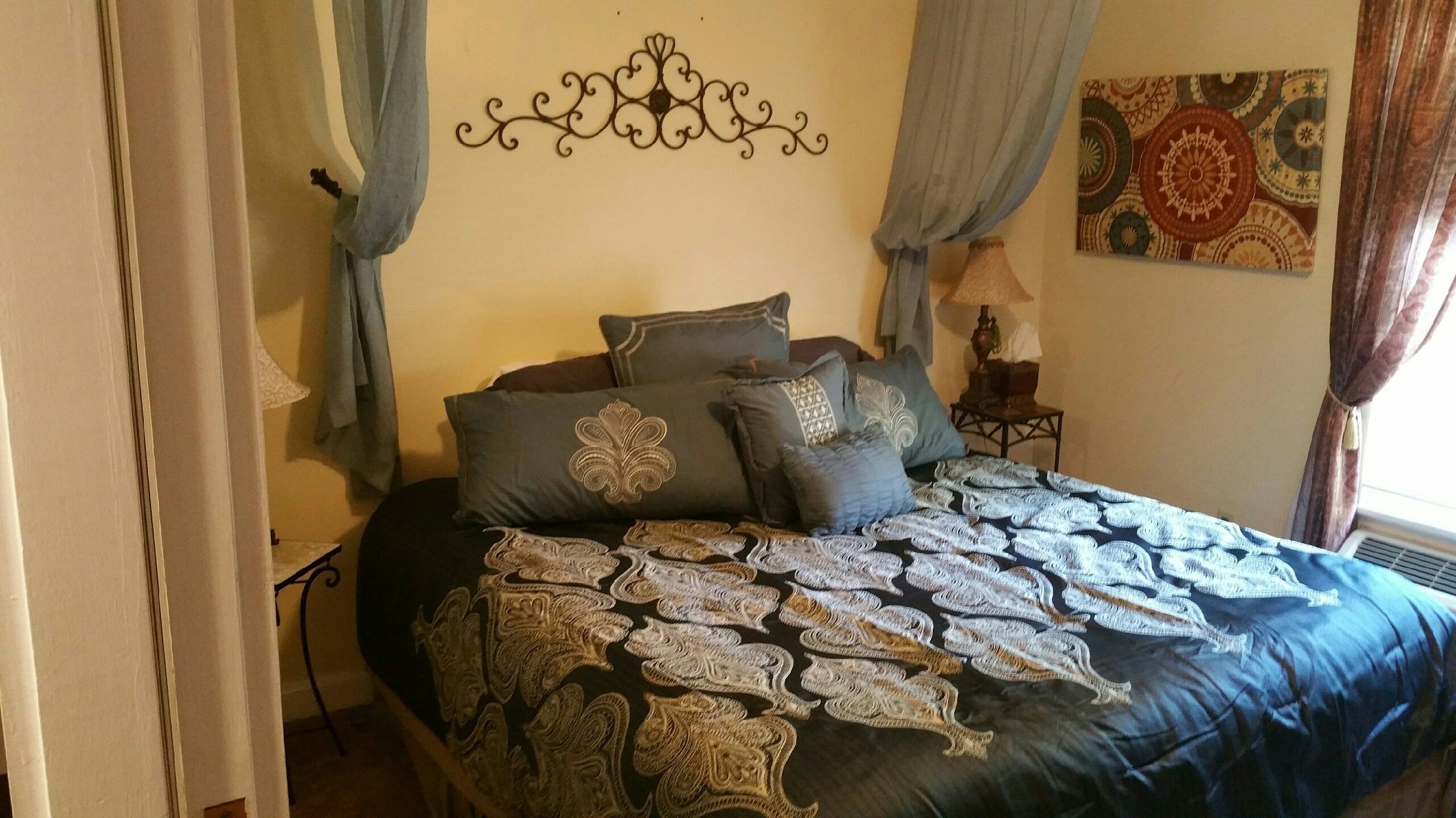 A bed with a patterned bedspread, multiple pillows, and a decorative wall hanging.