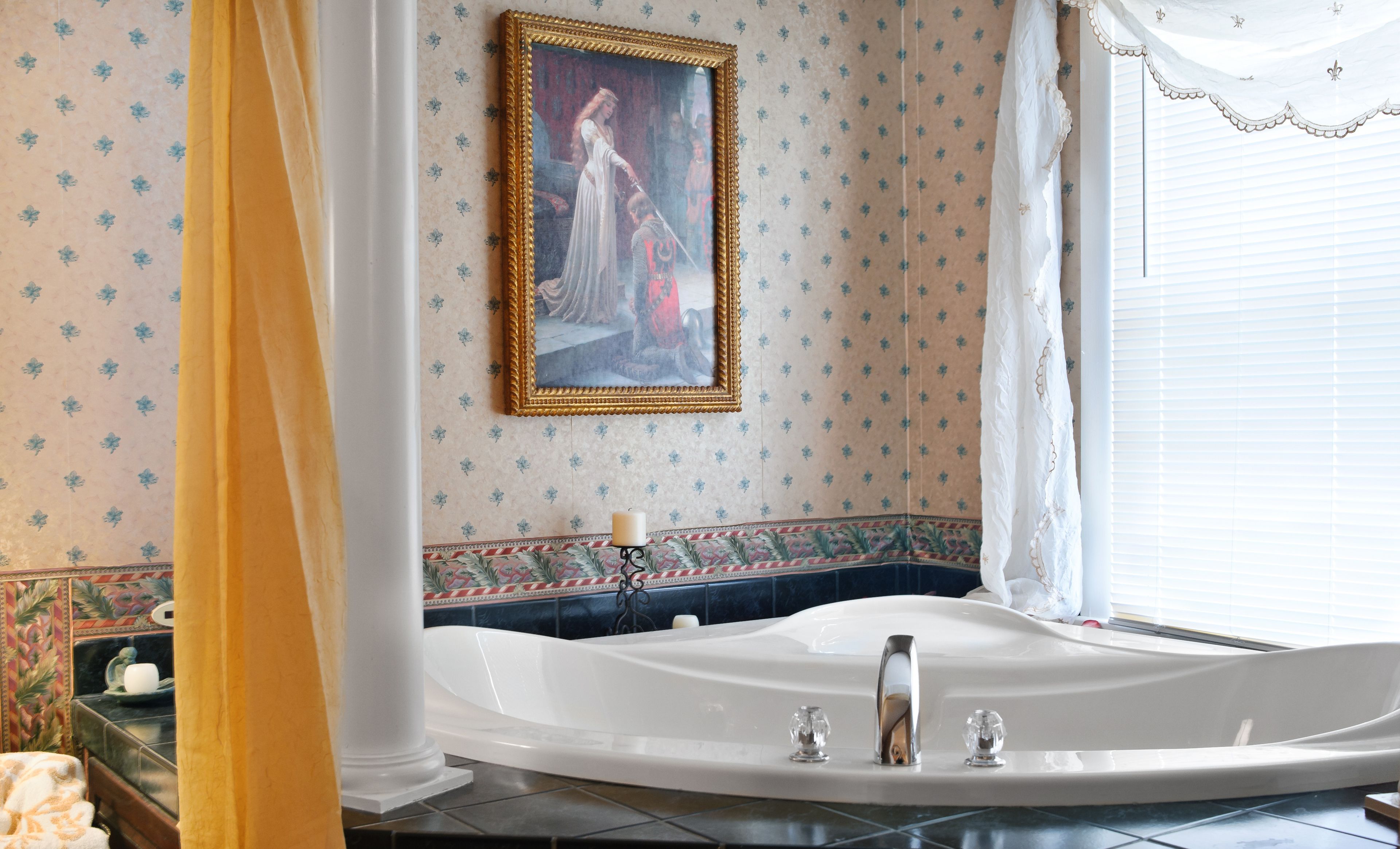 A bathroom with a large bathtub, a framed painting on the wall, and a window with curtains.