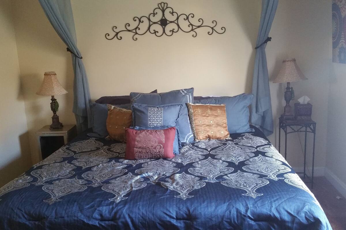 A bed with a blue patterned bedspread, multiple pillows, and a decorative headboard.