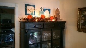 A kitchen with a cabinet displaying glassware and a decorative arrangement with pinecones and orange flowers. - Woodstock Inn B&B (Independence)