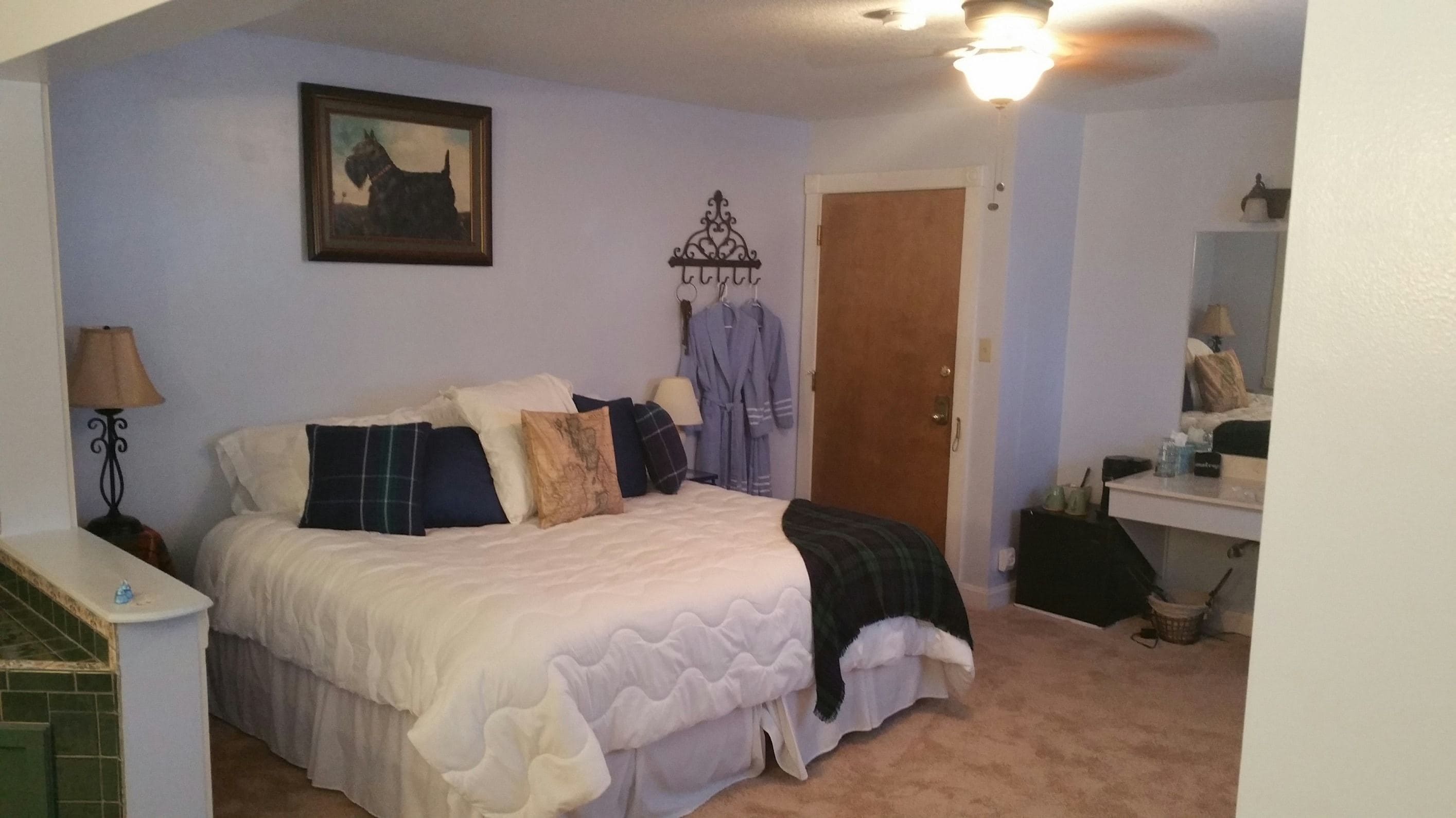 A bedroom with a bed, a framed picture, a robe rack, and a mirror.