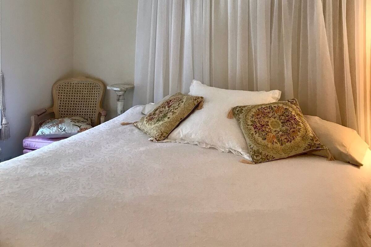 A bedroom with a canopy bed, two decorative pillows, a chair, and a nightstand.