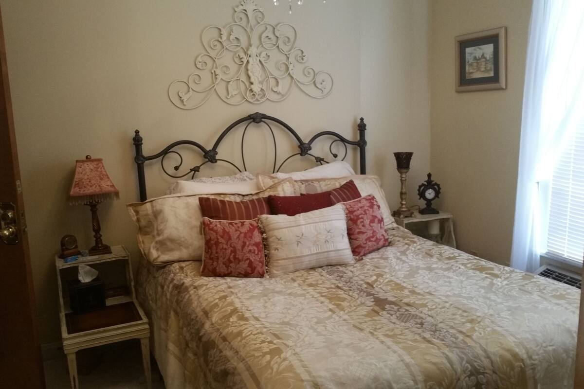 A bedroom with a bed, a nightstand, a lamp, a wall clock, and a decorative wall piece.
