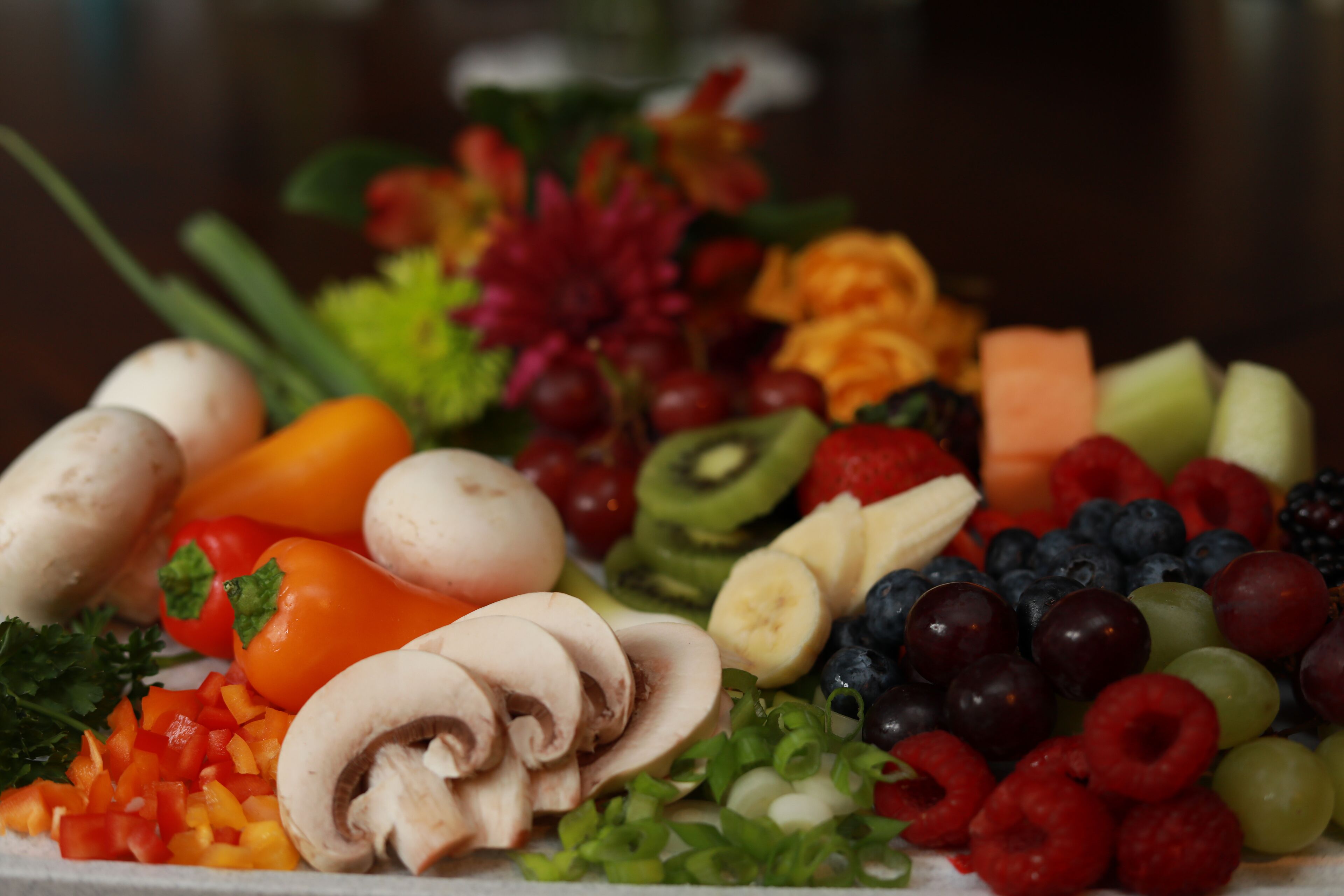 Uma travessa com uma variedade de frutas e legumes, incluindo pimentões, kiwi, uvas e cogumelos.