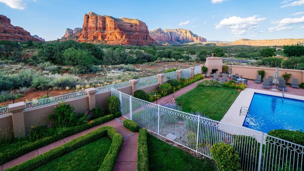 A resort with a swimming pool, manicured lawns, and a view of red rock formations.