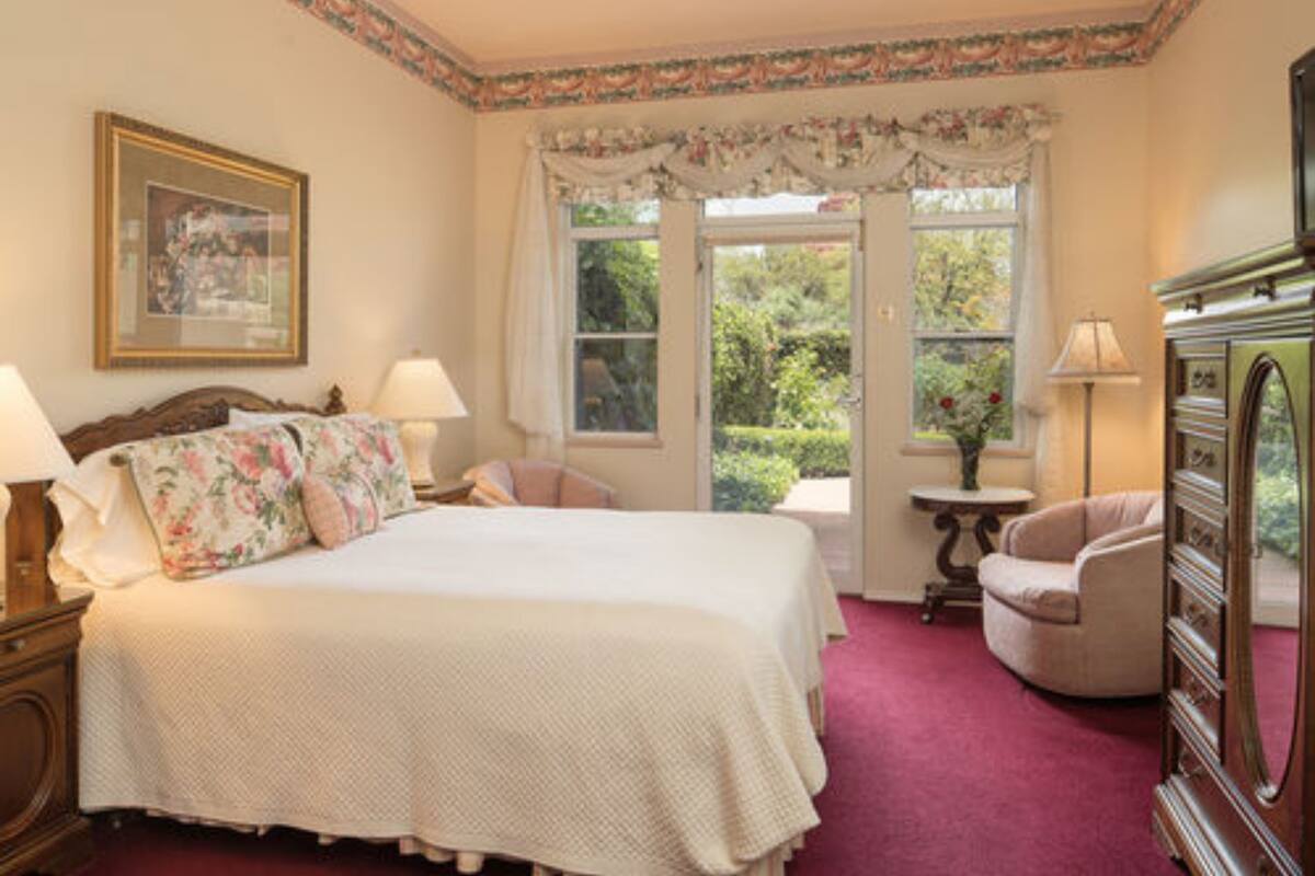 A bedroom with a large bed, two bedside tables, a chair, a dresser, and a window with curtains.