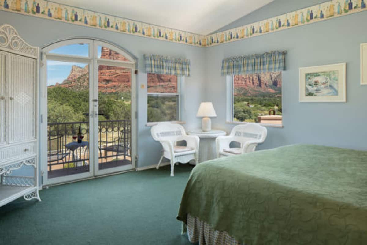 A room with a bed, two chairs, a table, and a view of red rock formations.