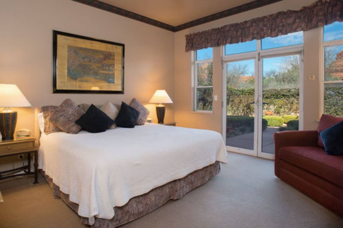 A bedroom with a large bed, two bedside tables, a red sofa, and a sliding glass door leading to a patio.