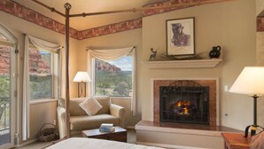 A cozy bedroom with a large bed, a fireplace, and a view of the outdoors.