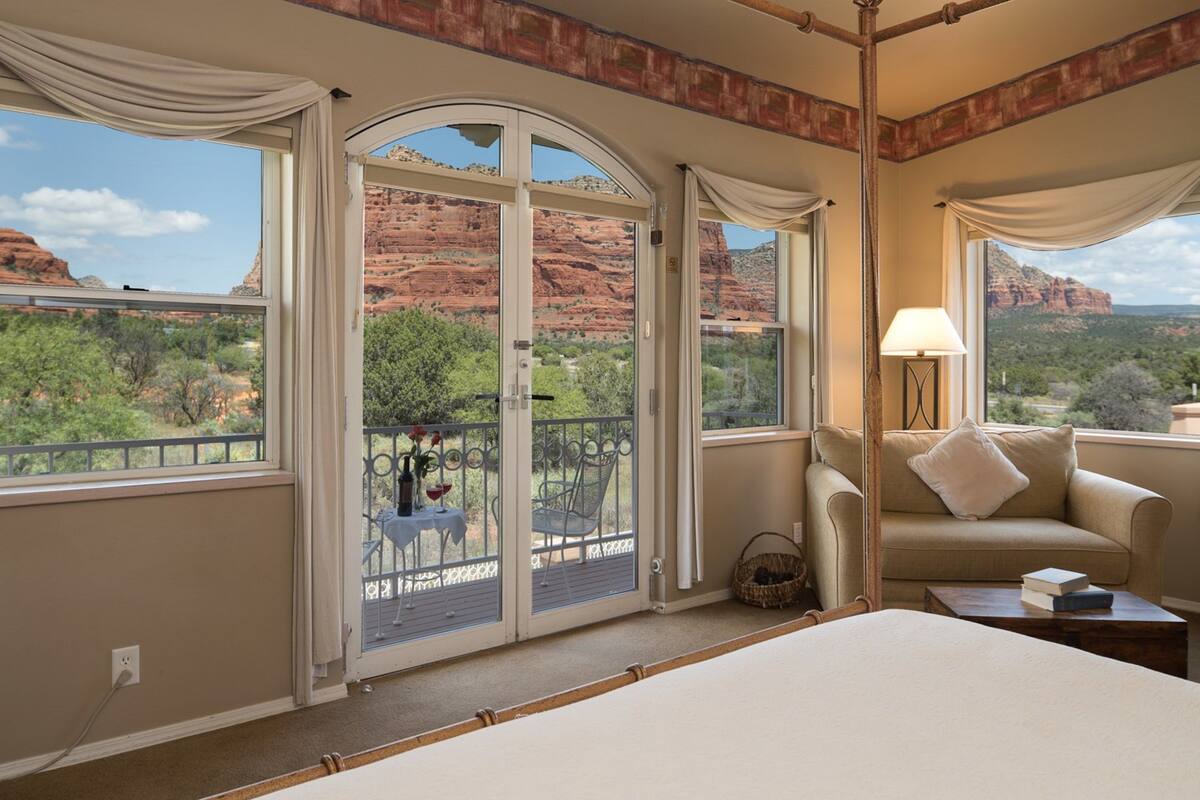 A room with a large sliding glass door leading to an outdoor balcony, a bed, a sofa, and a lamp.