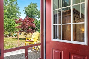 Une porte rouge avec une fenêtre, une terrasse en bois et une chaise jaune à l’extérieur.