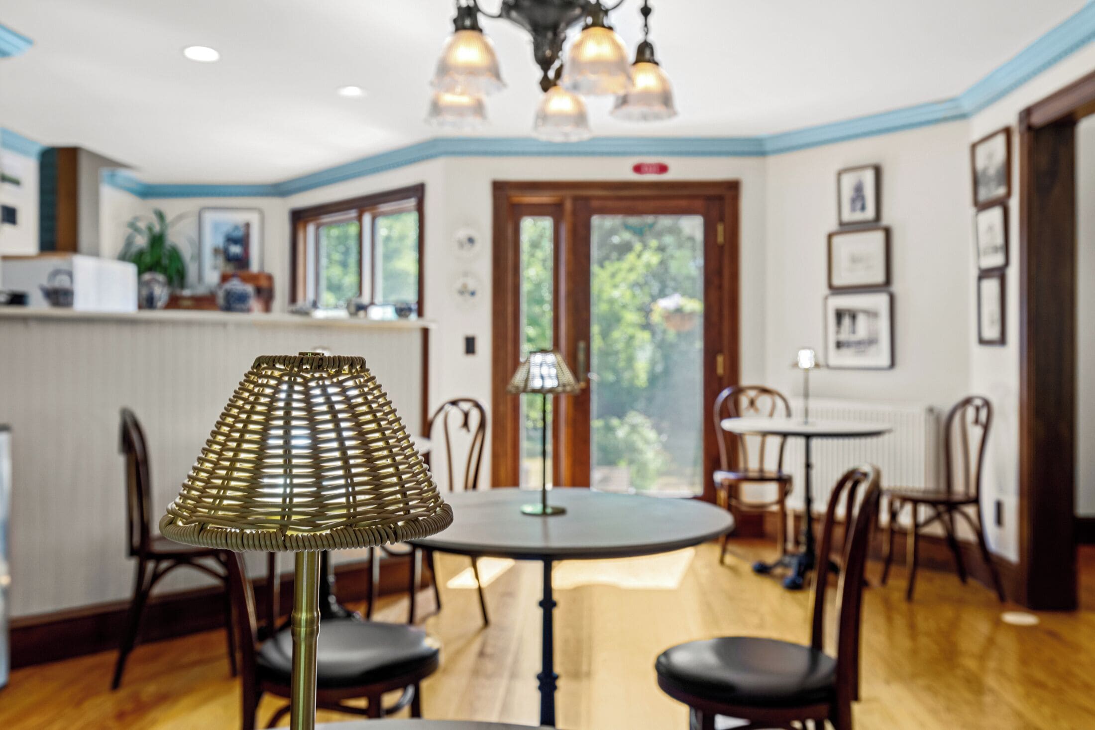 A dining area with a round table, chairs, a lamp, and a view through a door to the outside.
