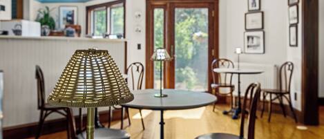 A dining area with a round table, chairs, a lamp, and a view through a door to the outside.