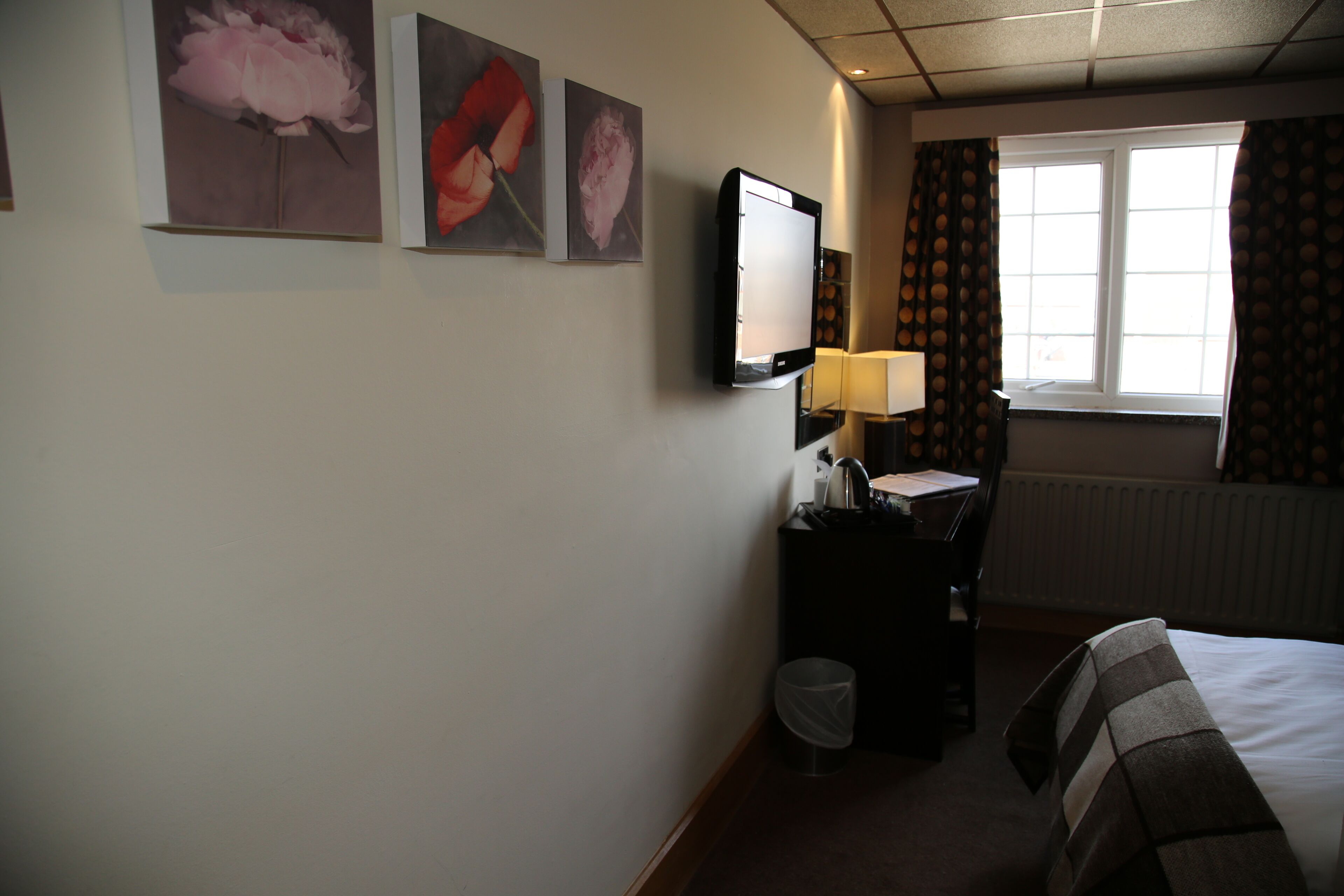 Ein Hotelzimmer mit einem Bett, einem Schreibtisch mit Computer, einem Stuhl, einer Lampe und drei gerahmten Bildern an der Wand.