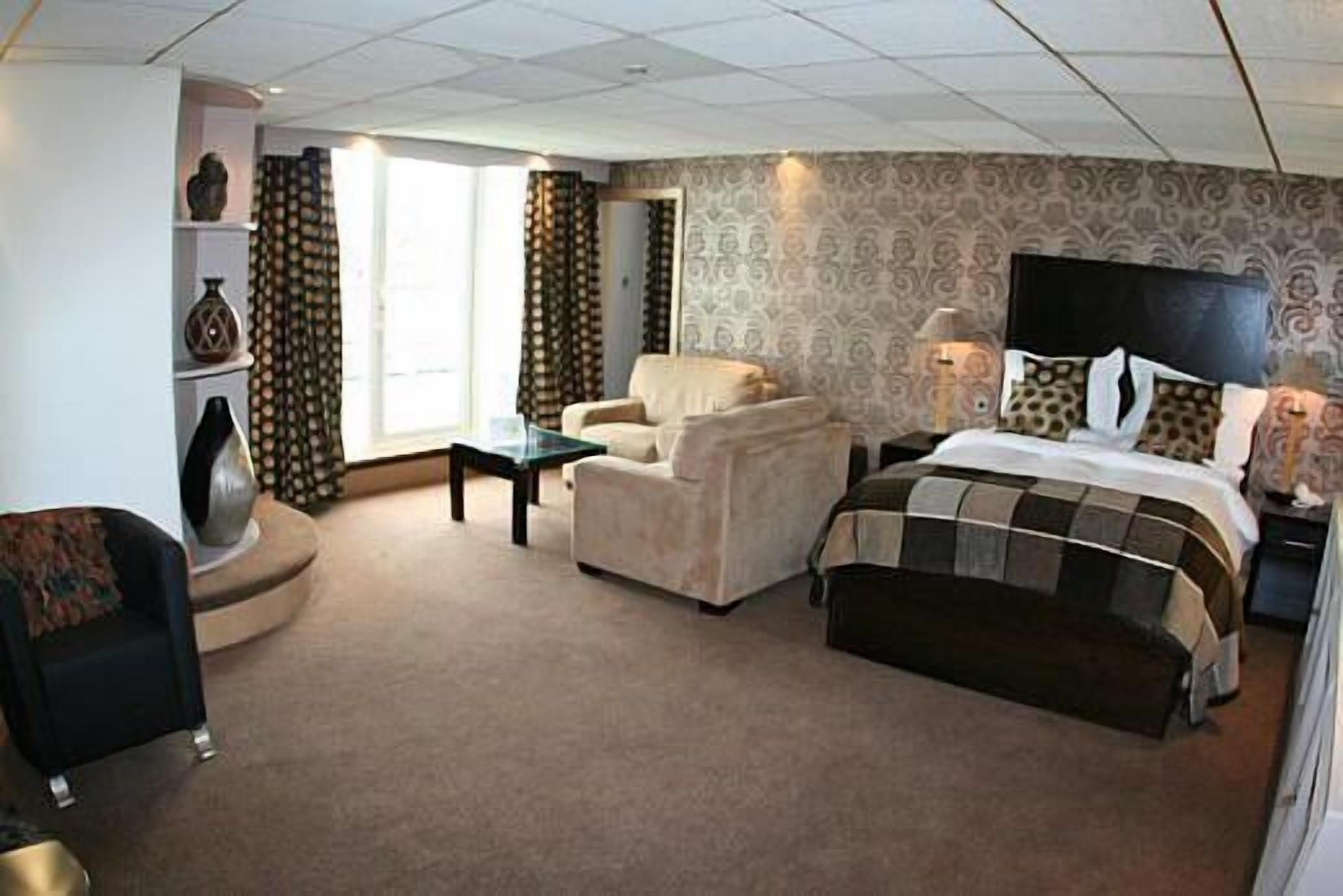 A hotel room with a bed, a chair, a desk, and a lamp.