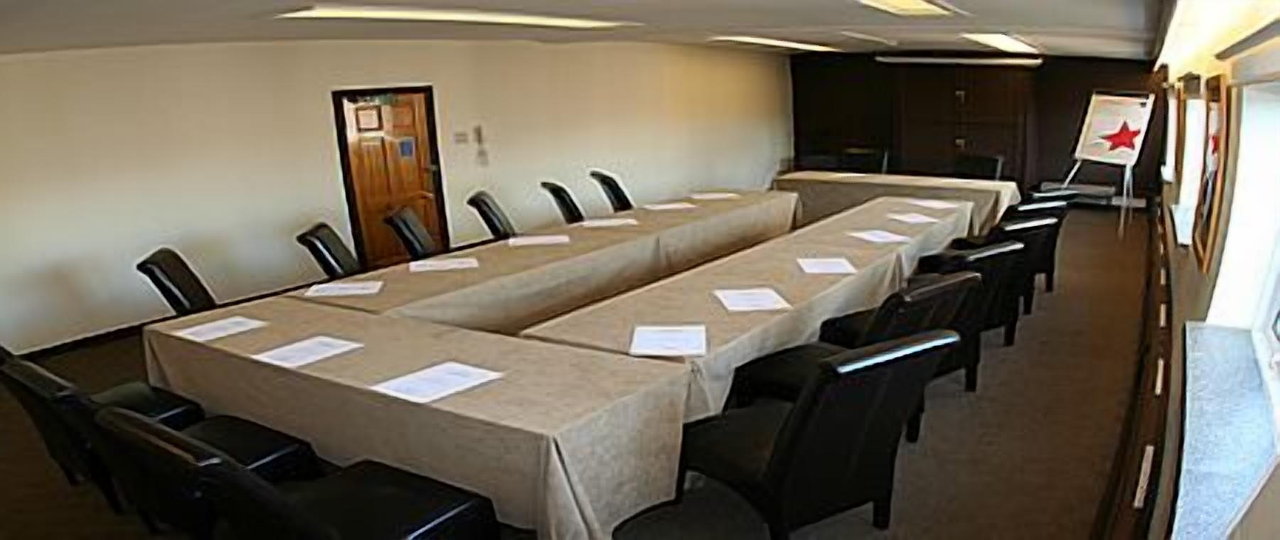 Une salle de conférence avec une longue table, des chaises et un drapeau accroché au mur.