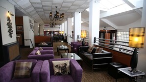 Un hall d’entrée spacieux, avec des canapés violets, une table basse et un lustre.