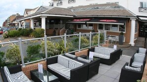 Un espace extérieur aménagé avec des canapés et des tables aux rayures noires et blanches, une terrasse couverte et un bâtiment sur lequel est apposée une enseigne indiquant « The Lodge ».