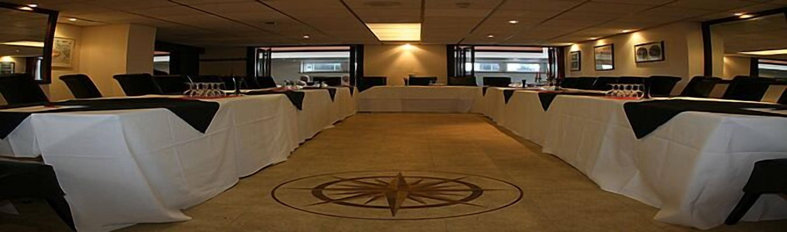 Een vergaderruimte met een lange tafel, witte tafelkleden en een kompasontwerp op het tapijt.