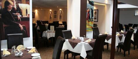 A restaurant with tables set for dining, framed artwork on the walls, and a patterned carpet.