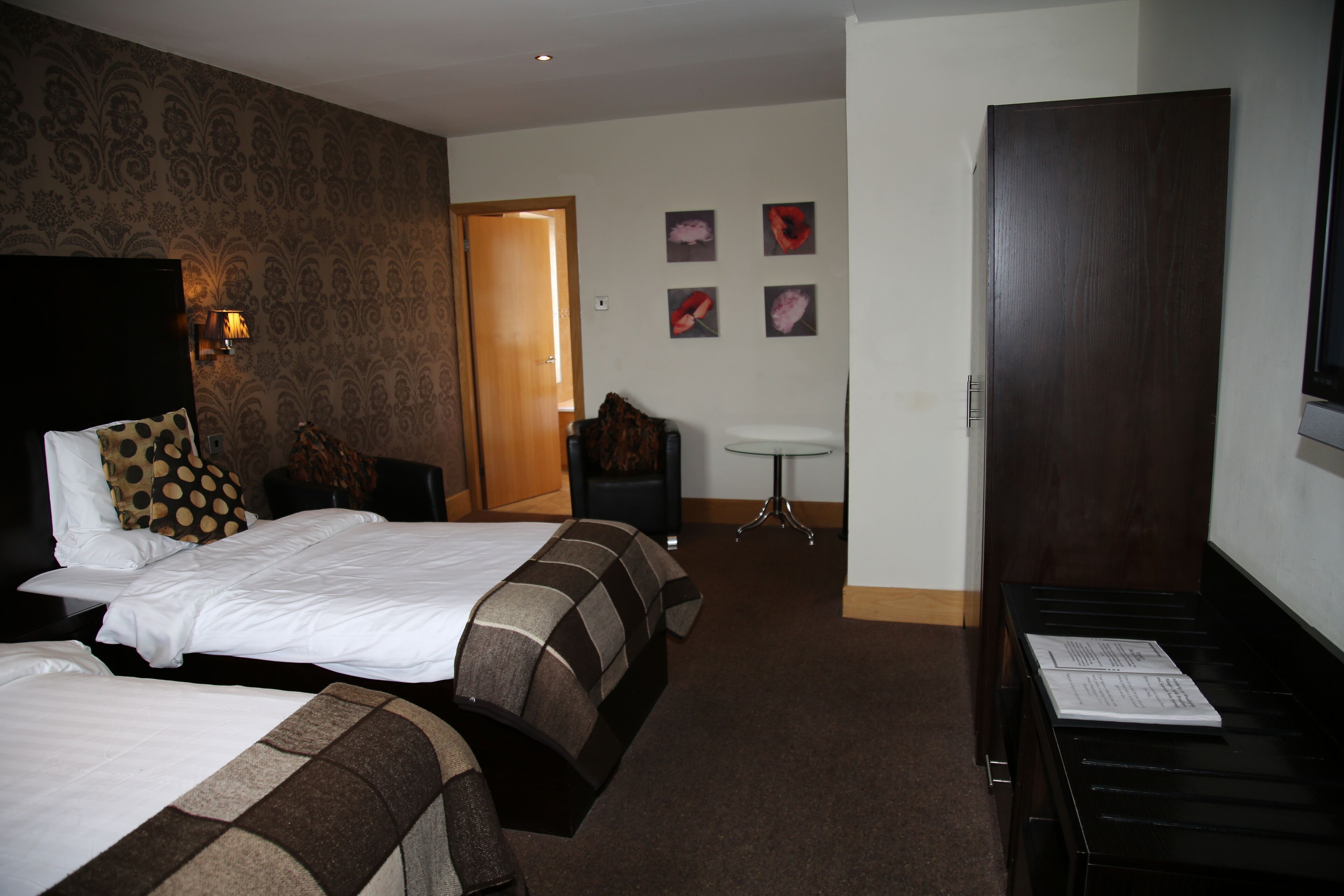 A hotel room with two beds, a desk, a chair, a small table, and a door.