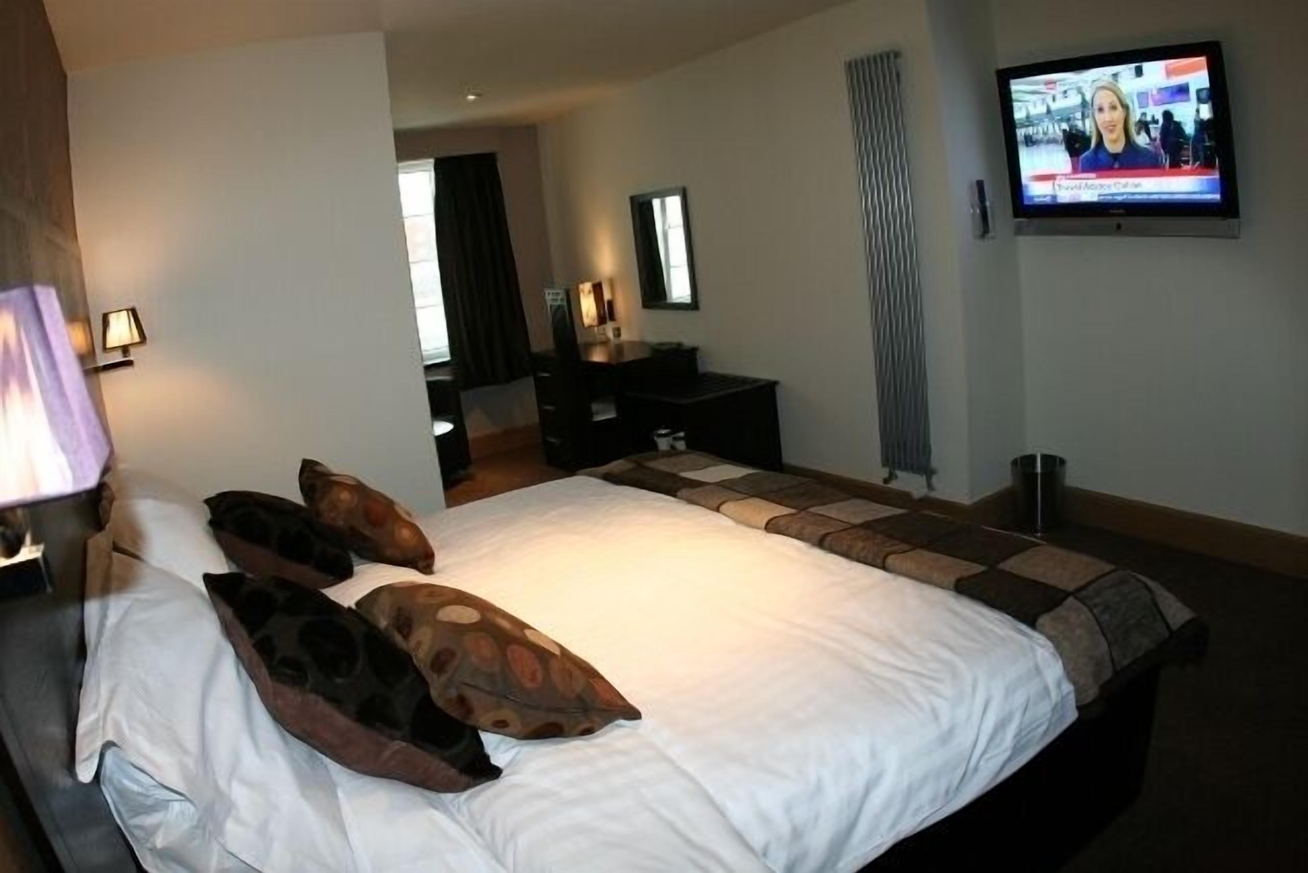Una habitación de hotel con una cama grande, un escritorio, un televisor y un espejo.