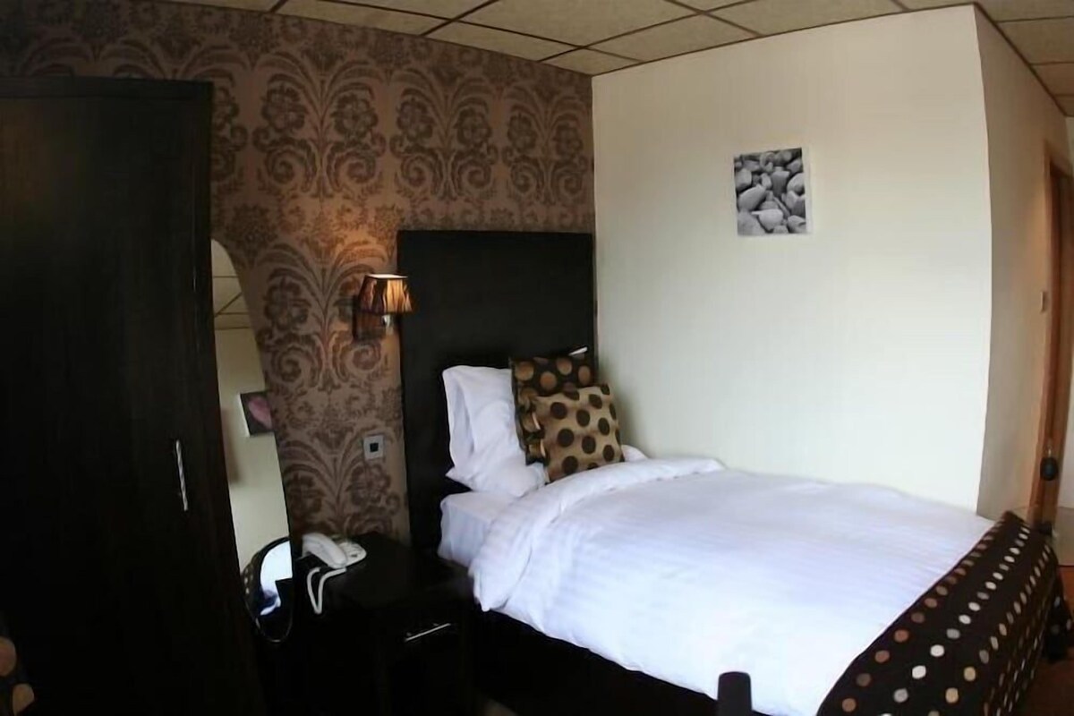 A hotel room with a bed, a nightstand, a lamp, and a patterned wallpaper.