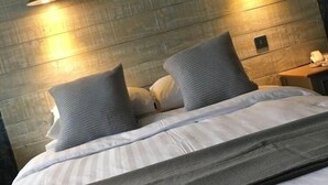 Un lit avec une couette rayée blanche et grise, deux oreillers gris et un plaid gris. Deux lampes murales sont fixées de chaque côté du lit.