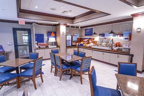 A hotel dining area with a buffet, seating arrangements, and a kitchen counter. - Holiday Inn Express and Suites Springfield Medical District by IHG (Springfield)