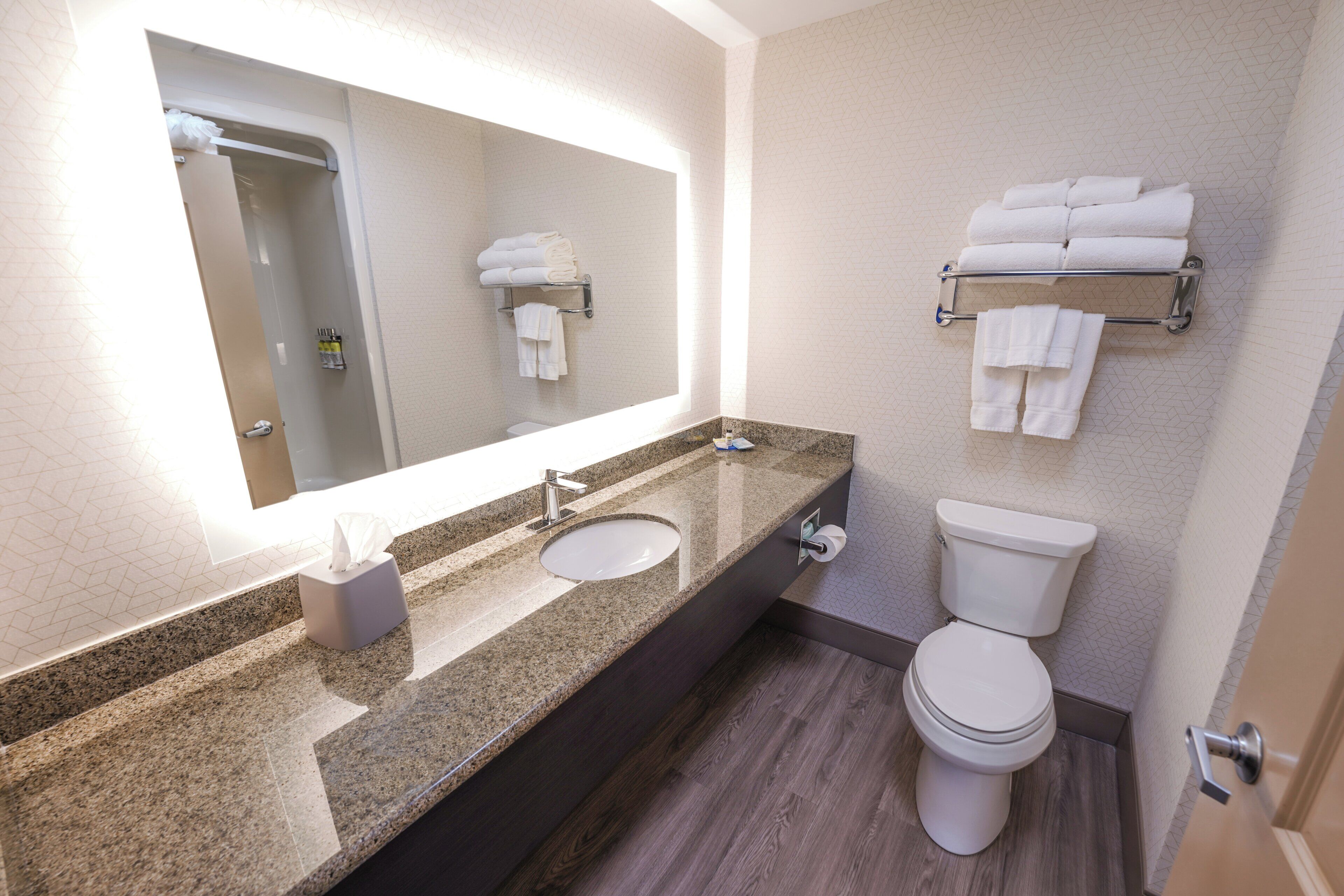 A bathroom with a large mirror, two sinks, a toilet, and towel racks.