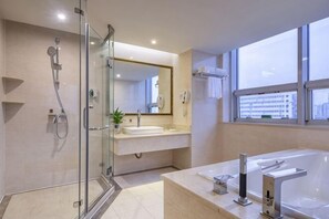 Un bagno moderno con box doccia in vetro, uno specchio grande, una vasca da bagno e una finestra con vista sulla città.