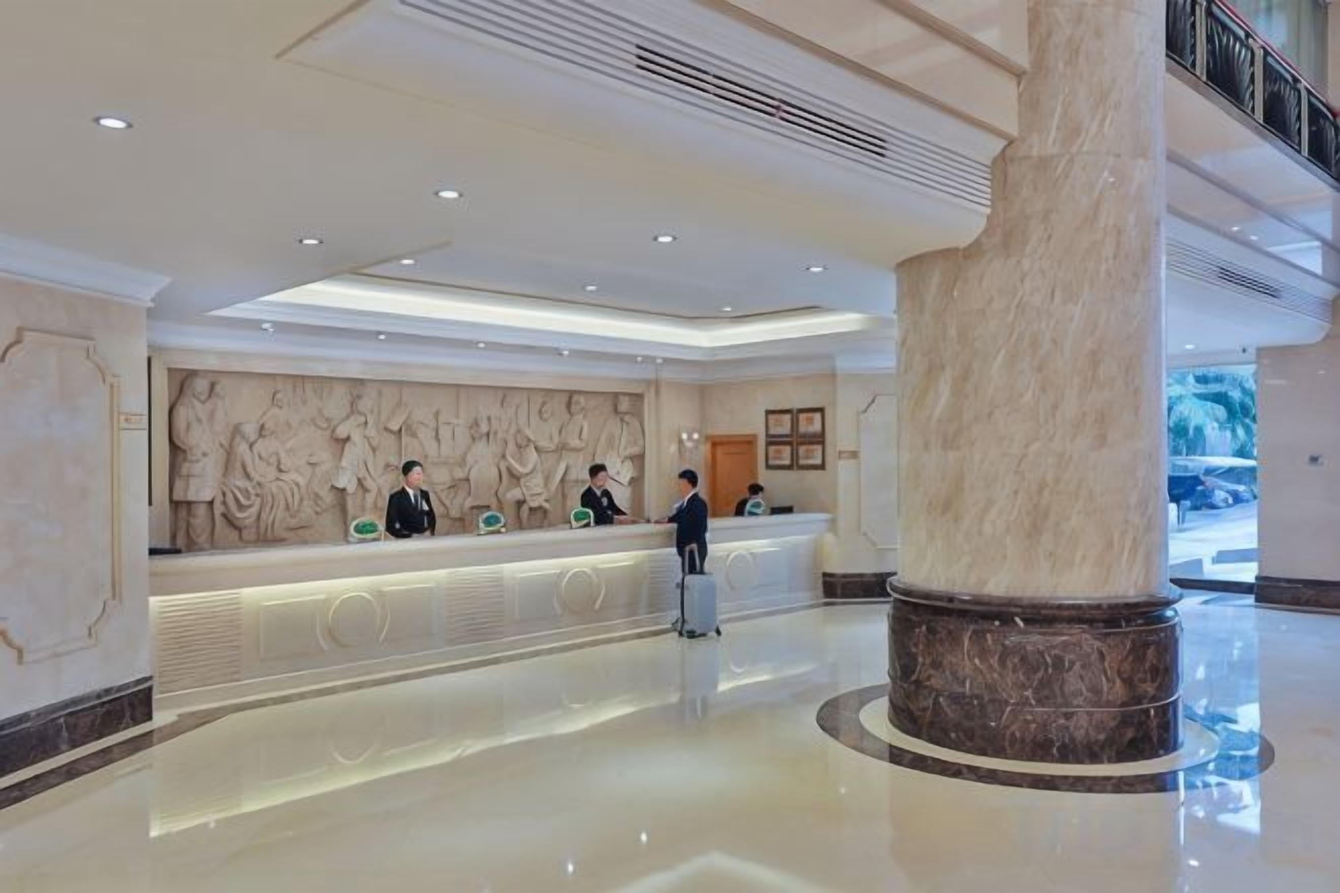 A hotel reception area with a marble reception desk, a large column, and a modern ceiling design.