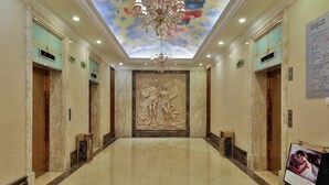 A hotel lobby with a marble floor, a chandelier, a ceiling mural, and a large wall sculpture. - Vienna International Hotel (Beijing Niujie Guang'anmennei Subway Station Branch) (Beijing)