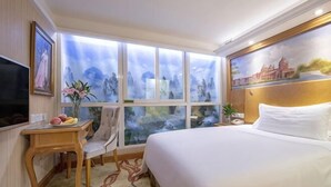 A hotel room with a bed, a desk with a chair, a TV, a window with a view, and a painting on the wall. - Vienna International Hotel (Beijing Niujie Guang'anmennei Subway Station Branch) (Beijing)