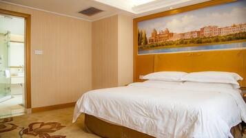 A hotel room with a bed, a painting of a cityscape, and a door leading to a bathroom.