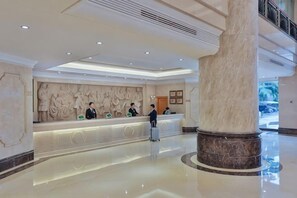 A hotel lobby with a marble reception desk, a large column, and a high ceiling with recessed lighting. - Vienna International Hotel (Beijing Niujie Guang'anmennei Subway Station Branch) (Beijing)