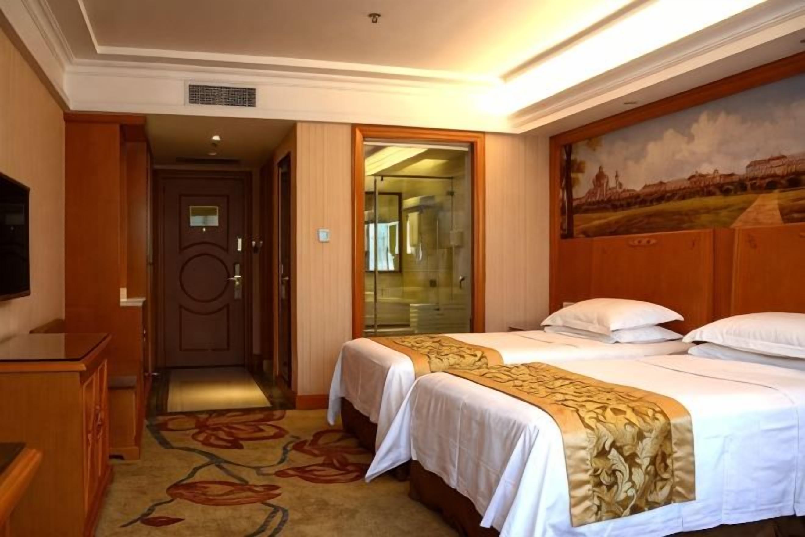 A hotel room with two beds, a television, and a painting on the wall.