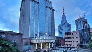 A modern hotel with a prominent glass facade, a classical entrance, and a parking lot with several cars. - Vienna International Hotel (Beijing Niujie Guang'anmennei Subway Station Branch) (Beijing)